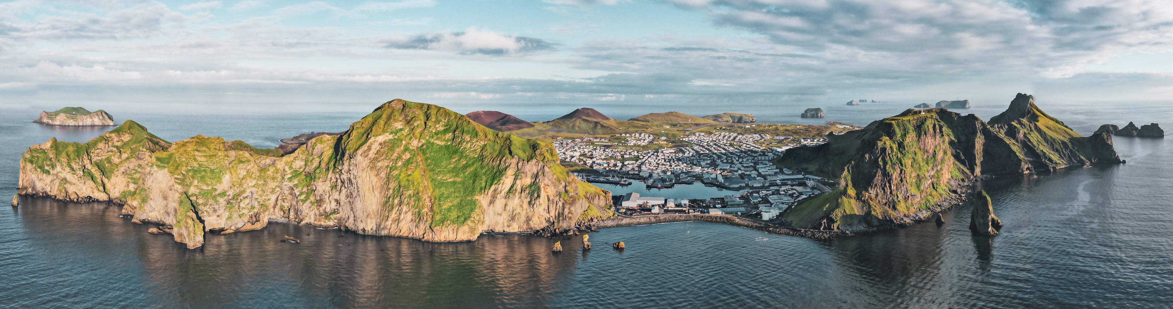 A stunning aerial view of Heimaey in the Westman Islands, showcasing the picturesque town, Eyðið, and the surrounding landscape, home to our exquisite gourmet flake salt harvested from the island's pristine waters.